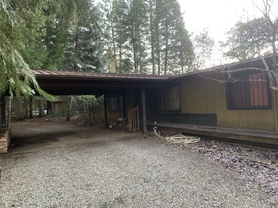 The residence and covered carport seen from the gravel drive